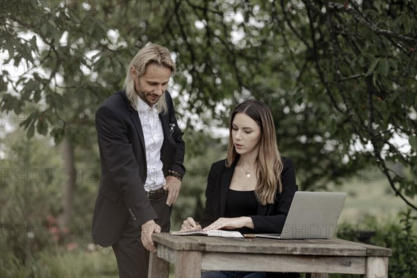 Businessman and businesswoman working in the open on a laptop at a wooden table