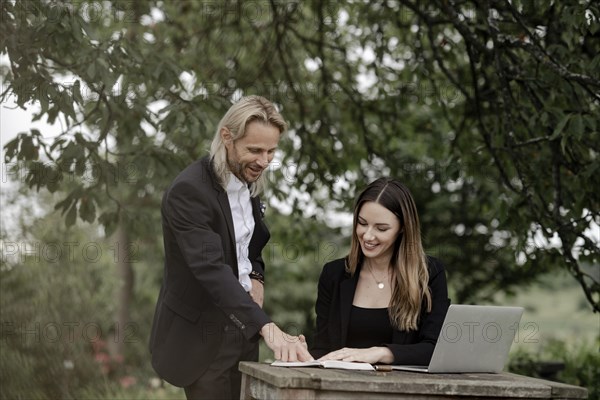 Businessman and businesswoman working in the open on a laptop at a wooden table