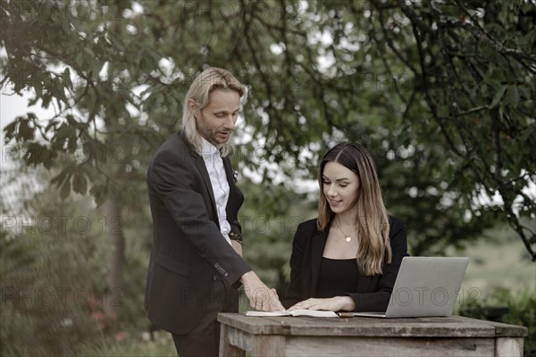 Businessman and businesswoman working in the open on a laptop at a wooden table