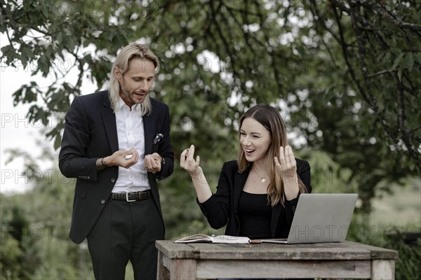 Businessman and businesswoman working in the open on a laptop at a wooden table