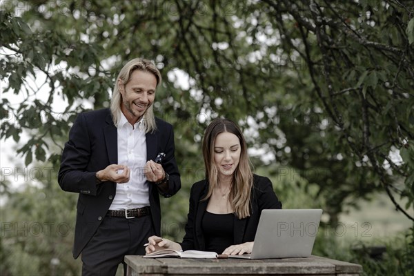 Businessman and businesswoman working in the open on a laptop at a wooden table