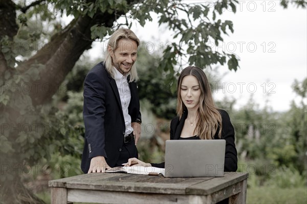 Businessman and businesswoman working in the open on a laptop at a wooden table