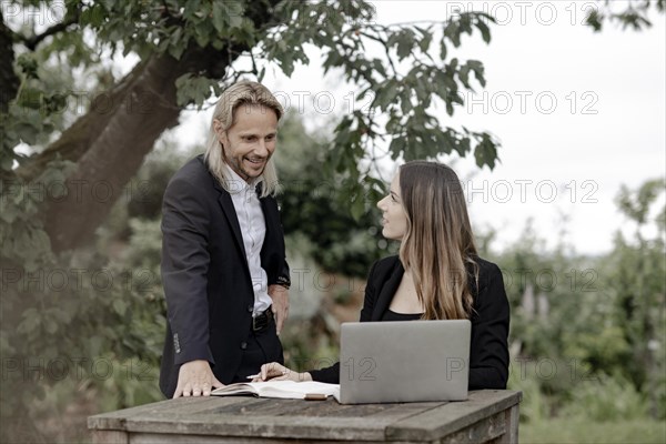 Businessman and businesswoman working in the open on a laptop at a wooden table