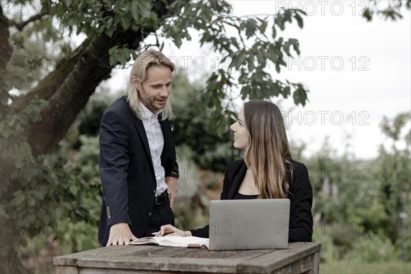 Businessman and businesswoman working in the open on a laptop at a wooden table