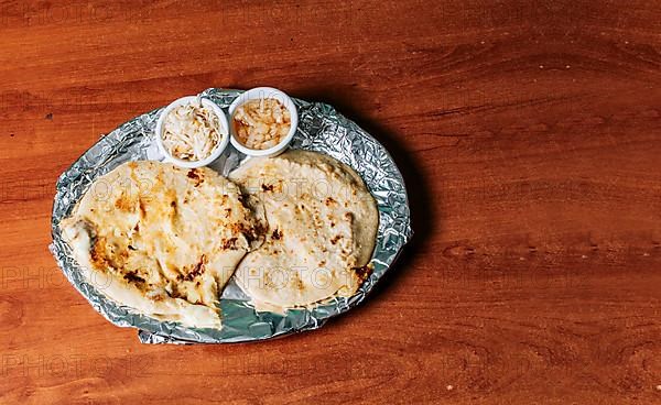 Traditional pupusas served with salad on the table. Top view of two Nicaraguan pupusas served with salad on the table. Delicious Salvadoran pupusas with melted cheese on wooden table