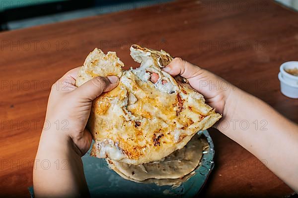 View of hands dividing delicious Salvadoran pupusas on wooden table. Concept of traditional handmade pupusas