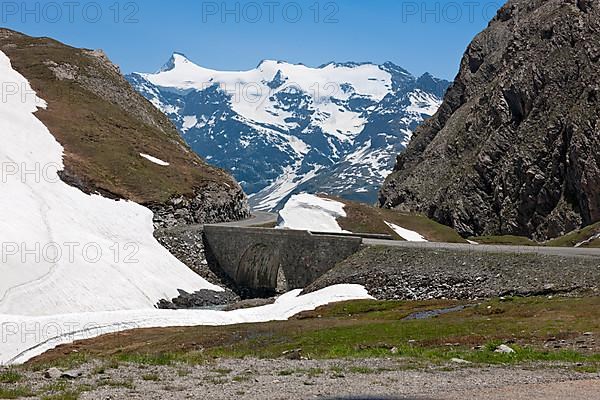 Bridge of mountain road in high Alps over glacier runoff of eternal snow melting in the background