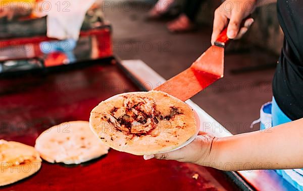 Hand holding a freshly made pupusa on a plate