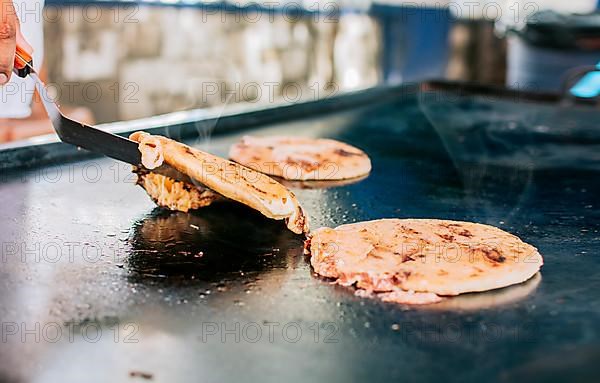 Spatula taking a traditional cheese pupusas on the grill