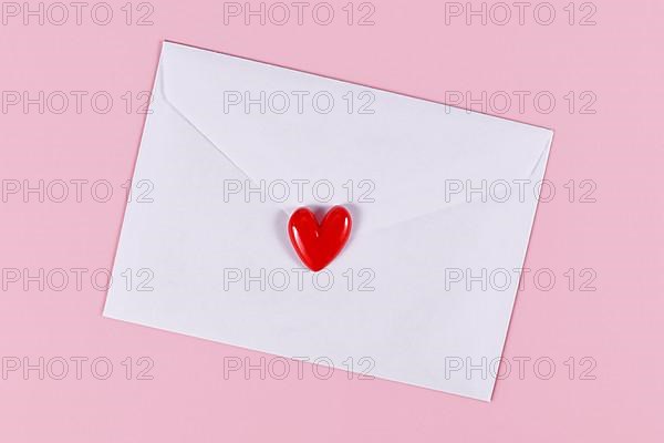 Love letter. White envelope with single red heart on pink background