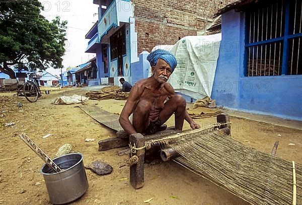 An old man weaving jute mats on the street at Tenkasi