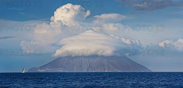 Sailing ship in front of Stromboli volcano and island with bizarre cloudscape