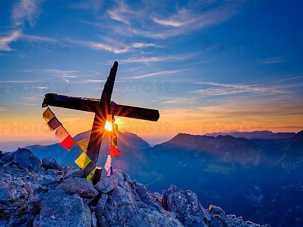 Buddhist prayer flags at the summit cross of the Kleiner Watzmann at sunrise