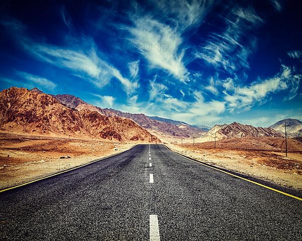 Vintage retro effect filtered hipster style image of road in mountains Himalayas and dramatic clouds on blue sky. Ladakh