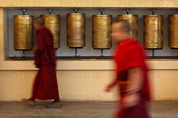 Buddhist monk passing and rotating prayer wheels on kora around Tsuglagkhang complex in McLeod Ganj