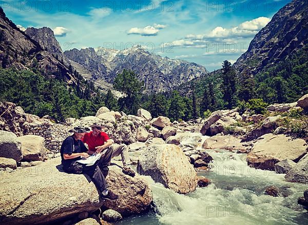 Vintage retro effect filtered hipster style image of hiker trekker tourists read a trekking map on trek in Himalayas mountains. Himachal Pradesh