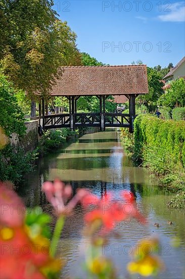 View of a covered wooden footbridge with flowers in the foreground