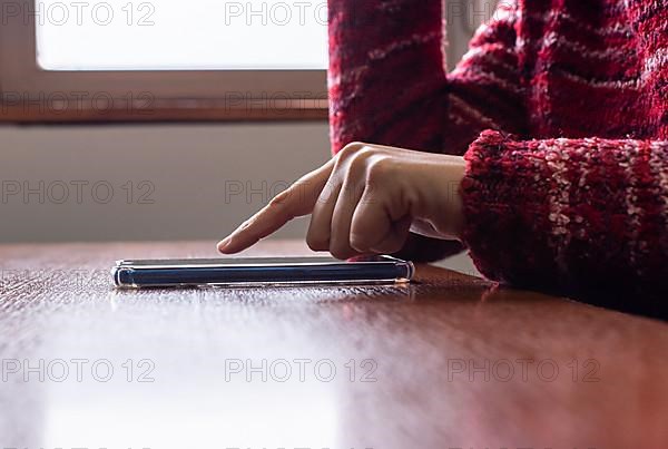 Side view of female hand using her smartphone touch screen near the window