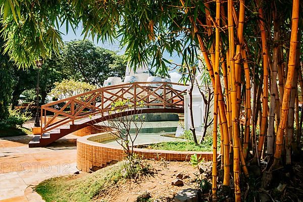 Wooden bridge in a park over water fountain surrounded by bamboo. Side view of a small wooden bridge over a water fountain in a calm park. Nagarote central park