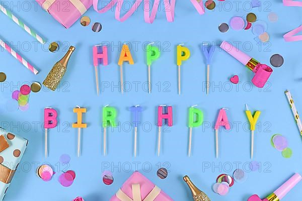 Letter canles forming text Happy Birthday with confetti and paper streamers on blue background