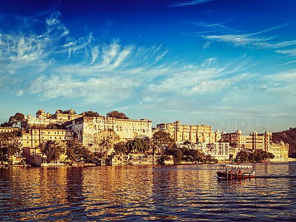 Vintage retro effect filtered hipster style image of City Palace and tourist boat on lake Pichola on sunset. Udaipur