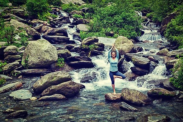 Vintage retro effect hipster style image of woman practices balance yoga asana Vrikshasana tree pose at waterfall outdoors. Himachal Pradesh