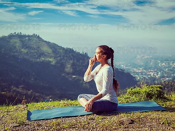 Vintage retro effect hipster style image of woman practices pranayama yoga breath control in lotus pose padmasana outdoors in Himalayas in the morning on sunrise. Himachal Pradesh