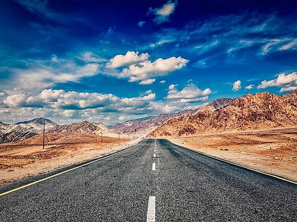 Vintage retro effect filtered hipster style image of road in mountains Himalayas and dramatic clouds on blue sky. Ladakh