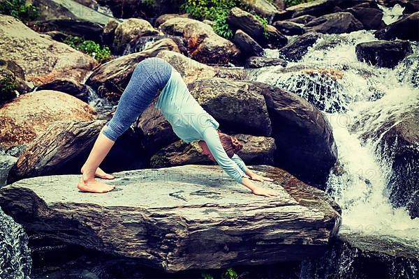 Vintage retro effect hipster style image of sporty fit woman doing yoga asana Adho mukha svanasana