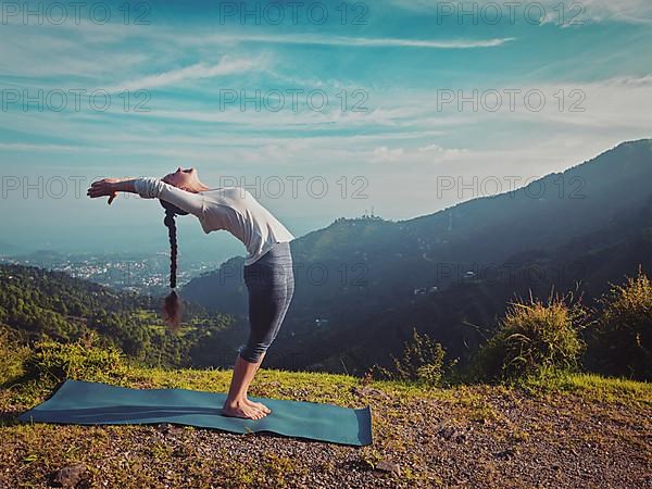 Vintage retro effect hipster style image of young sporty fit man doing yoga Sun salutation Surya Namaskar pose Hasta Uttanasana outdoors in mountains