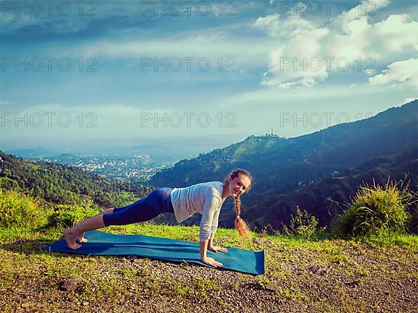 Vintage retro effect hipster style image of woman doing Hatha yoga asana Kumbhakasana plank pose outdoors in mountains