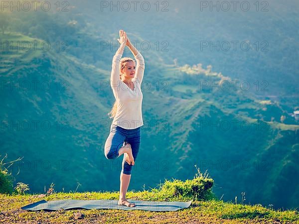 Vintage retro effect hipster style image of woman practices balance yoga asana Vrikshasana tree pose in Himalayas mountains outdoors in the morning. Himachal Pradesh