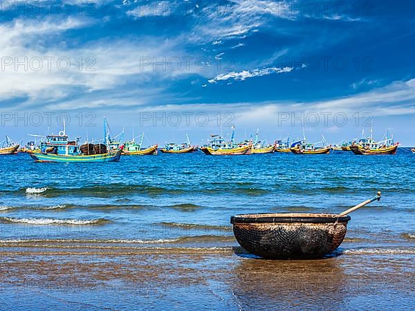 Coracle and fishing boats on beach in Mui Ne