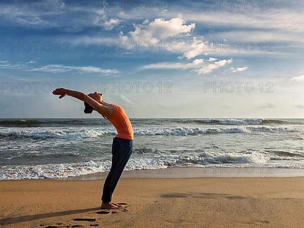 Young sporty fit woman doing yoga Sun salutation Surya Namaskar pose Hasta Uttanasana on tropical beach on sunset