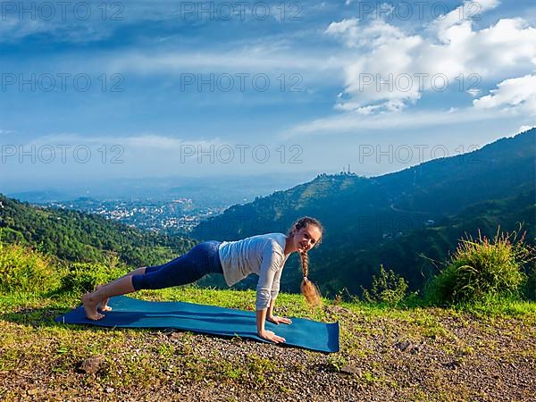 Woman doing Hatha yoga asana Kumbhakasana plank pose outdoors in mountains