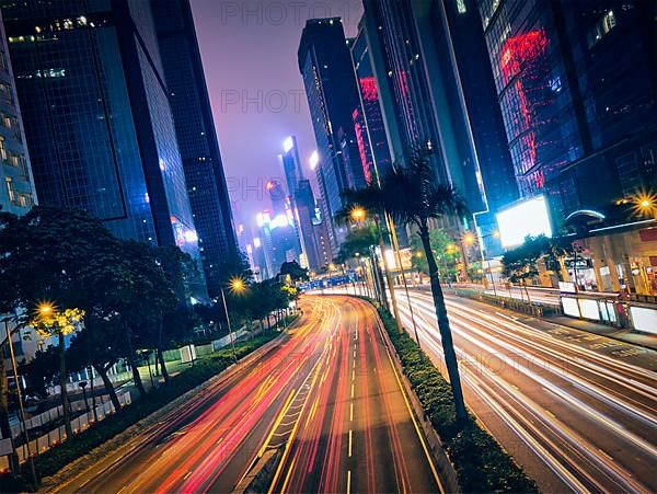 Street traffic in Hong Kong at night. Office skyscraper buildings and busy traffic on highway road with blurred cars light trails. Hong Kong