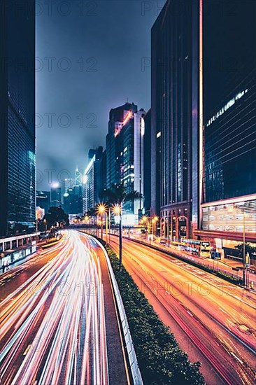 Street traffic in Hong Kong at night. Office skyscraper buildings and busy traffic on highway road with blurred cars light trails. Hong Kong