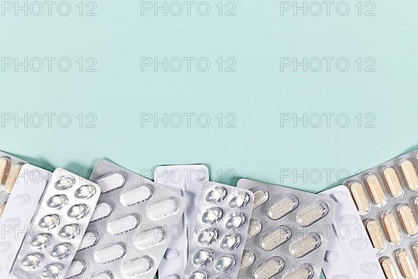 Blister packs with various pills and capsules at bottom of mint green background with copy space
