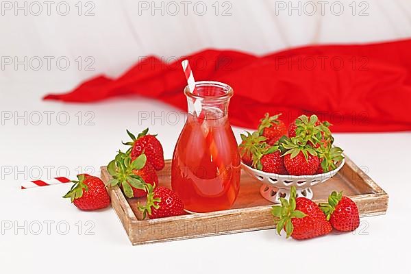 Strawberry fruit lemonade in jar surrounded by berries on wooden tray