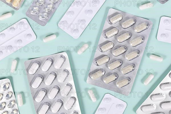 Various blister packs with pills and capsules on mint green background