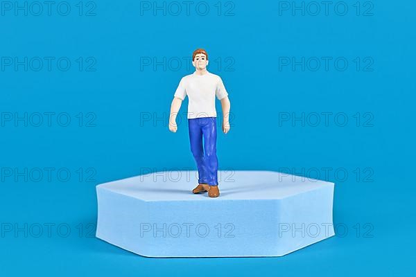 Man figure with shirt and jeans on pedestal in front of blue background