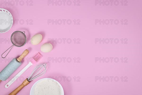 Cake dough ingredients and baking tools on pink background with copy space