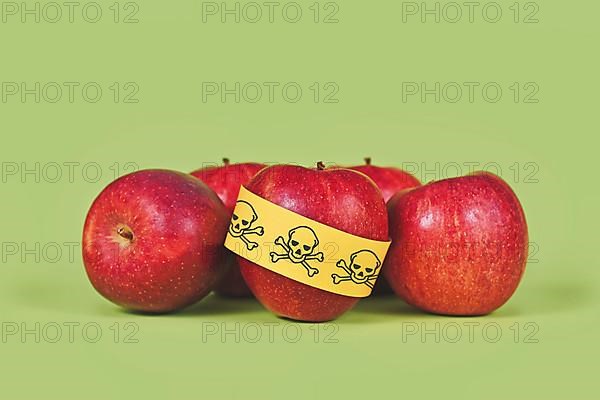 Apples with poison skull symbol sticker on green background. Concept of pesticide residues in agricultural food