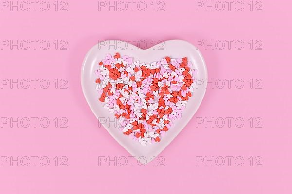 Plate with heart shaped sugar sprinkles on pink background