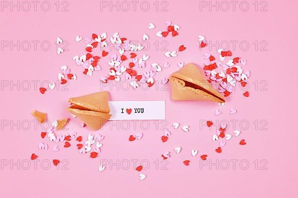 Fortune cookies with text 'I love you' and sugar sprinkle hearts on pink background