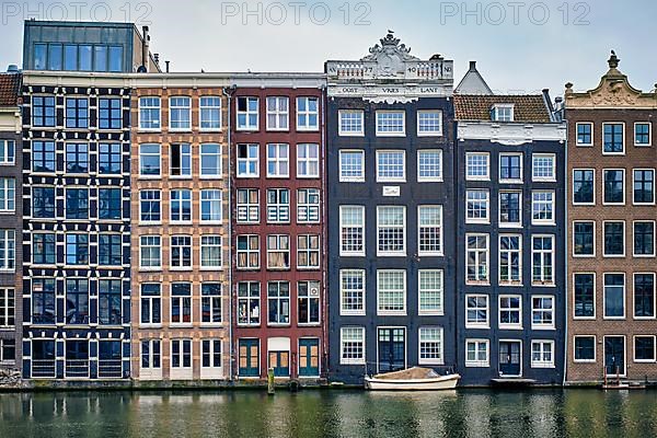 Row of typical houses and boat on Amsterdam canal Damrak with reflection. Amsterdam