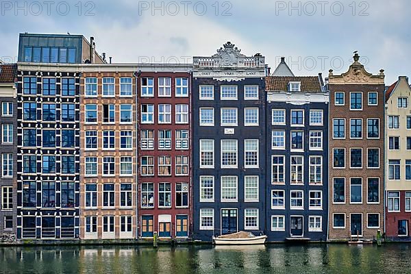 Row of typical houses and boat on Amsterdam canal Damrak with reflection. Amsterdam