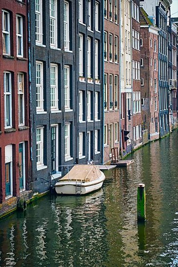 Row of typical houses and boat on Amsterdam canal Damrak with reflection. Amsterdam