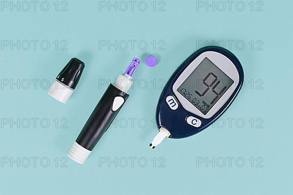 Tools for diabetes treatment with blood glucose sugar meter showing blood sugar of 94 and lancing device with lancet on blue background