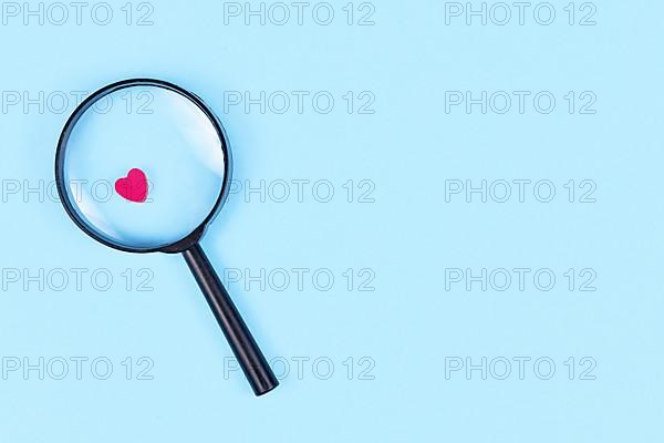 Looking for love concept with magnifier glass and pink heart icon on blue background with copy space